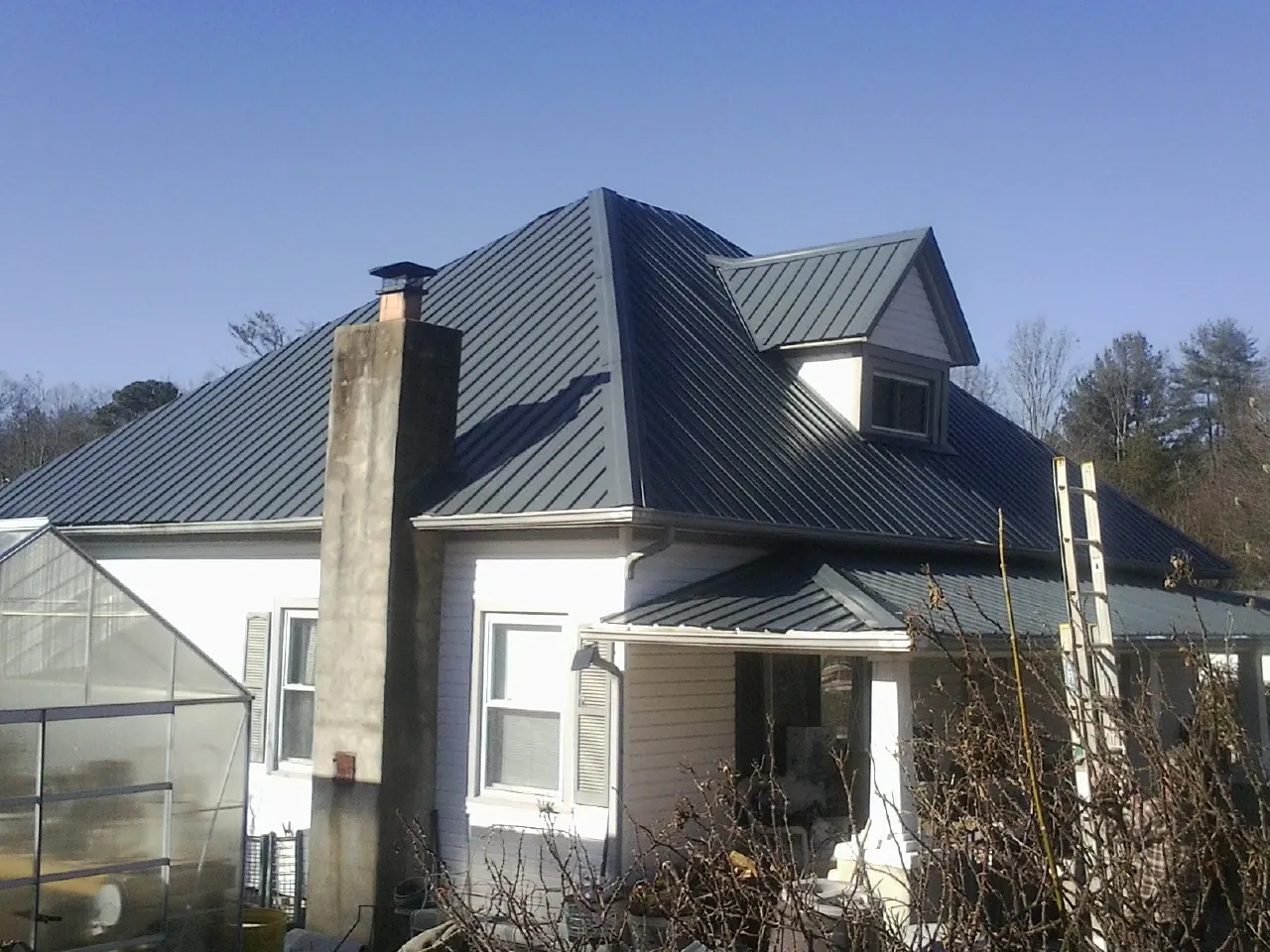 Dark blue standing seam metal roof on a white farmhouse with dormer — Slate & Tile Roof Repair by Roofing Brothers in Carmel By The Sea