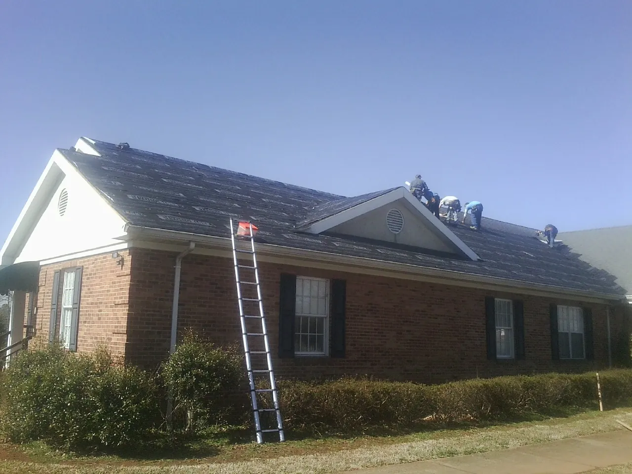 Crew tearing shingles off a brick ranch roof with a ladder set — Emergency Roof Repair work by our crew in Carmel By The Sea
