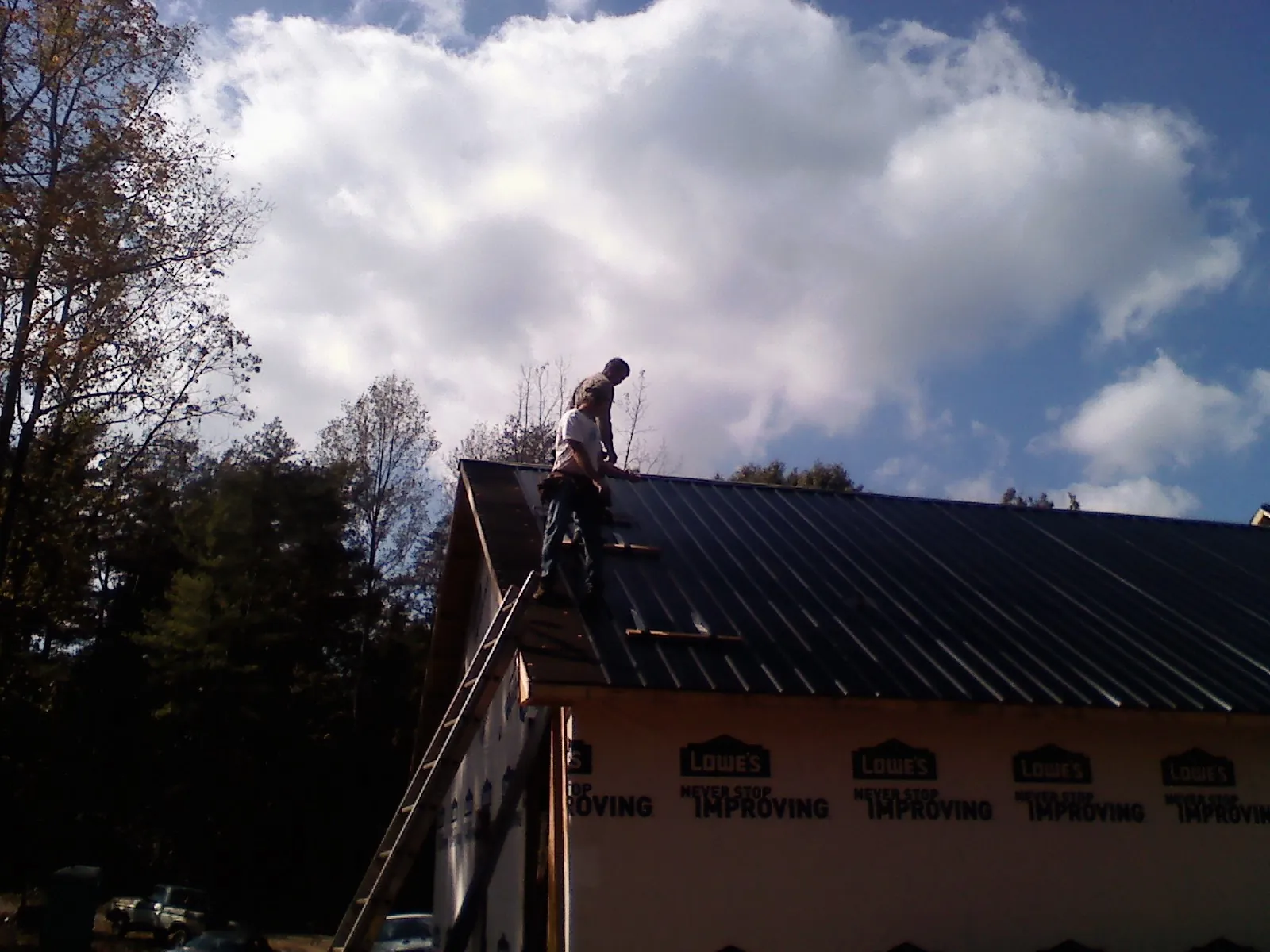 Roofer fastening dark metal panels high against a cloudy sky, from a Roof Inspection job in Carmel By The Sea