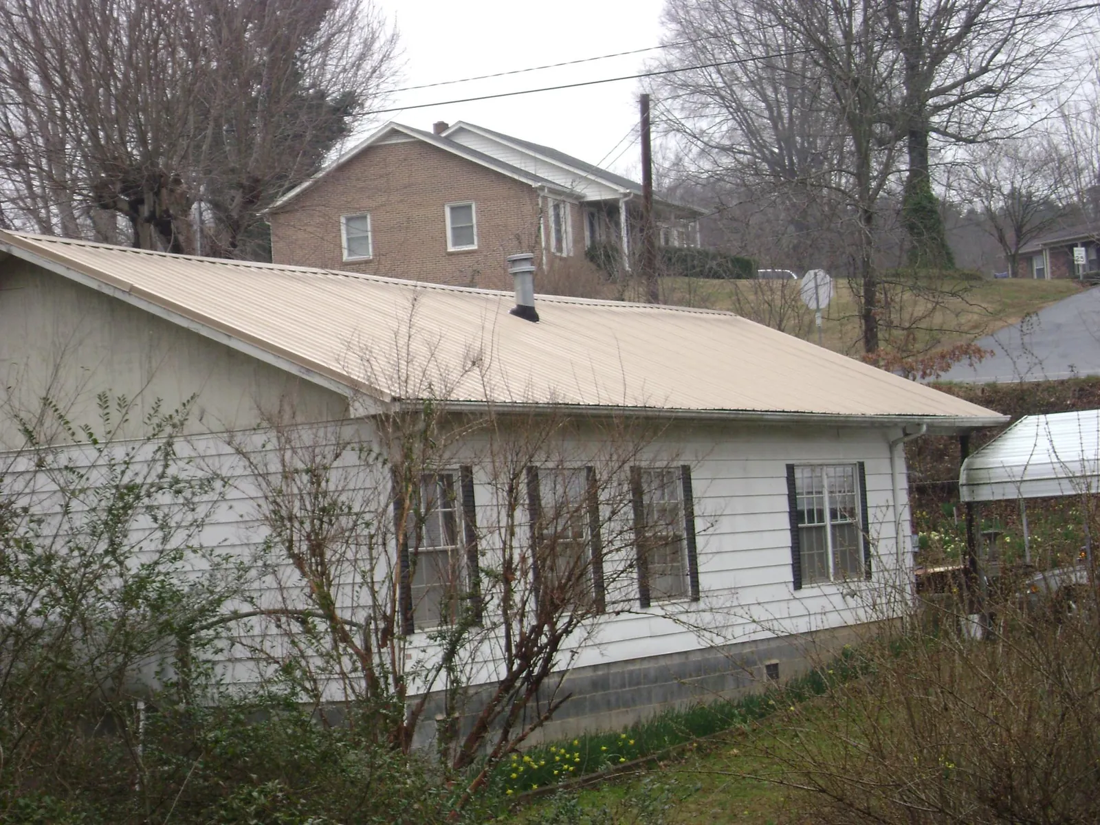 Tan metal roof on a white sided house set into a hillside — Commercial Roofing by Roofing Brothers in Carmel By The Sea